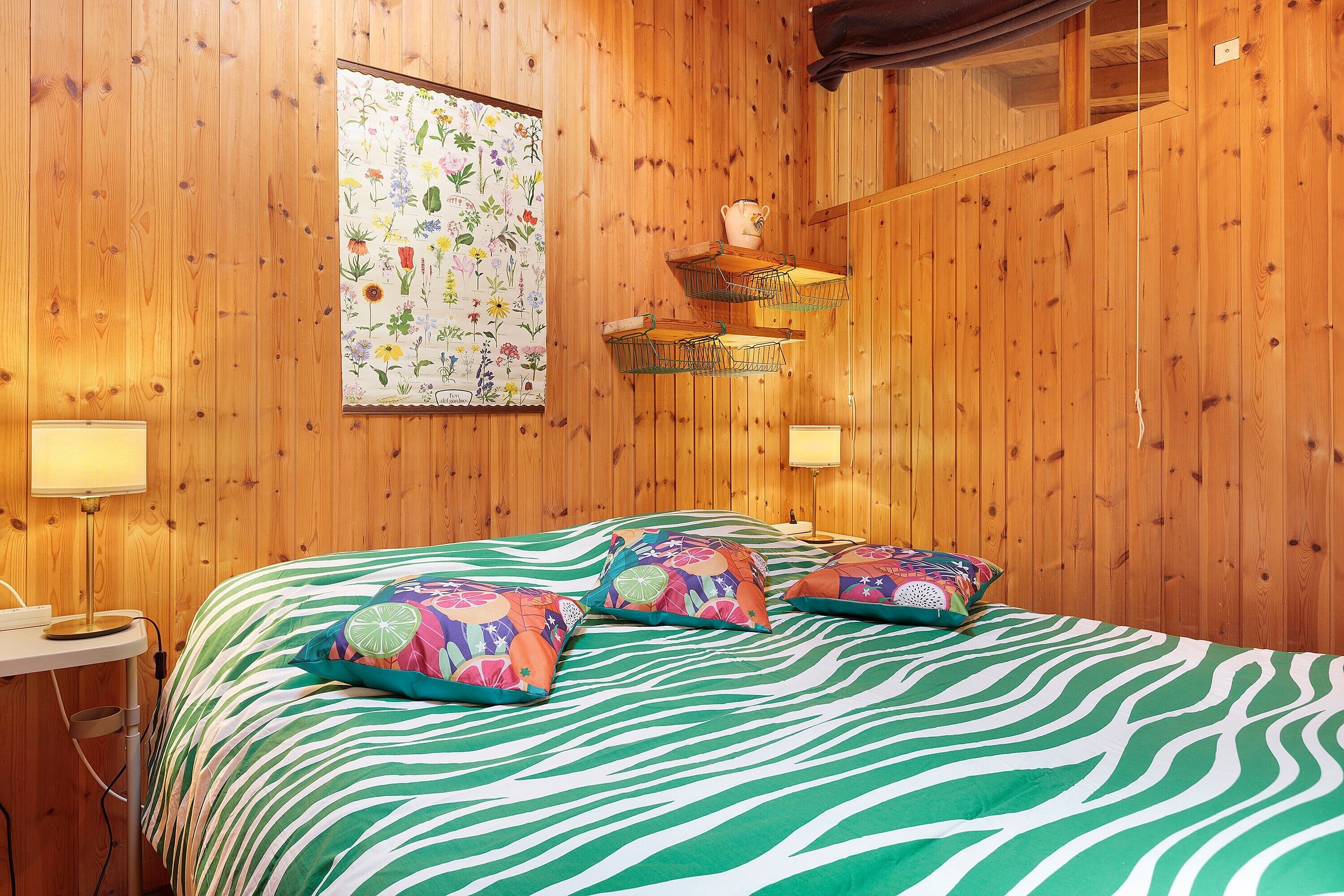 A wooden-paneled room with a zebra-striped bedspread, a floral poster, and a shelf with a teapot.