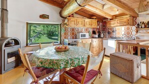 Een landelijke keuken met houten balken, een groot raam en een eethoek met een tafel en stoelen.