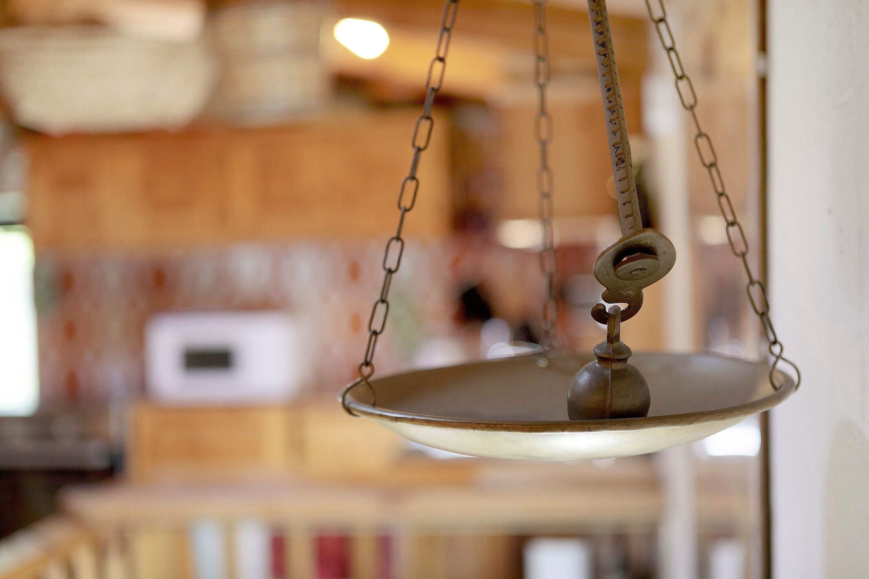 A hanging scale with a chain and a metal plate, suspended from a ceiling in a room with wooden walls and a window.