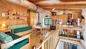 Een houten hut interieur met stapelbedden, een eettafel, stoelen, een keukenhoek en een grote balk.