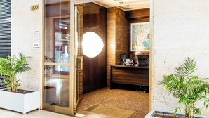 A reception area with a desk, a chair, a glass door, and a plant. - Suiteincenter Rooms (Palermo)