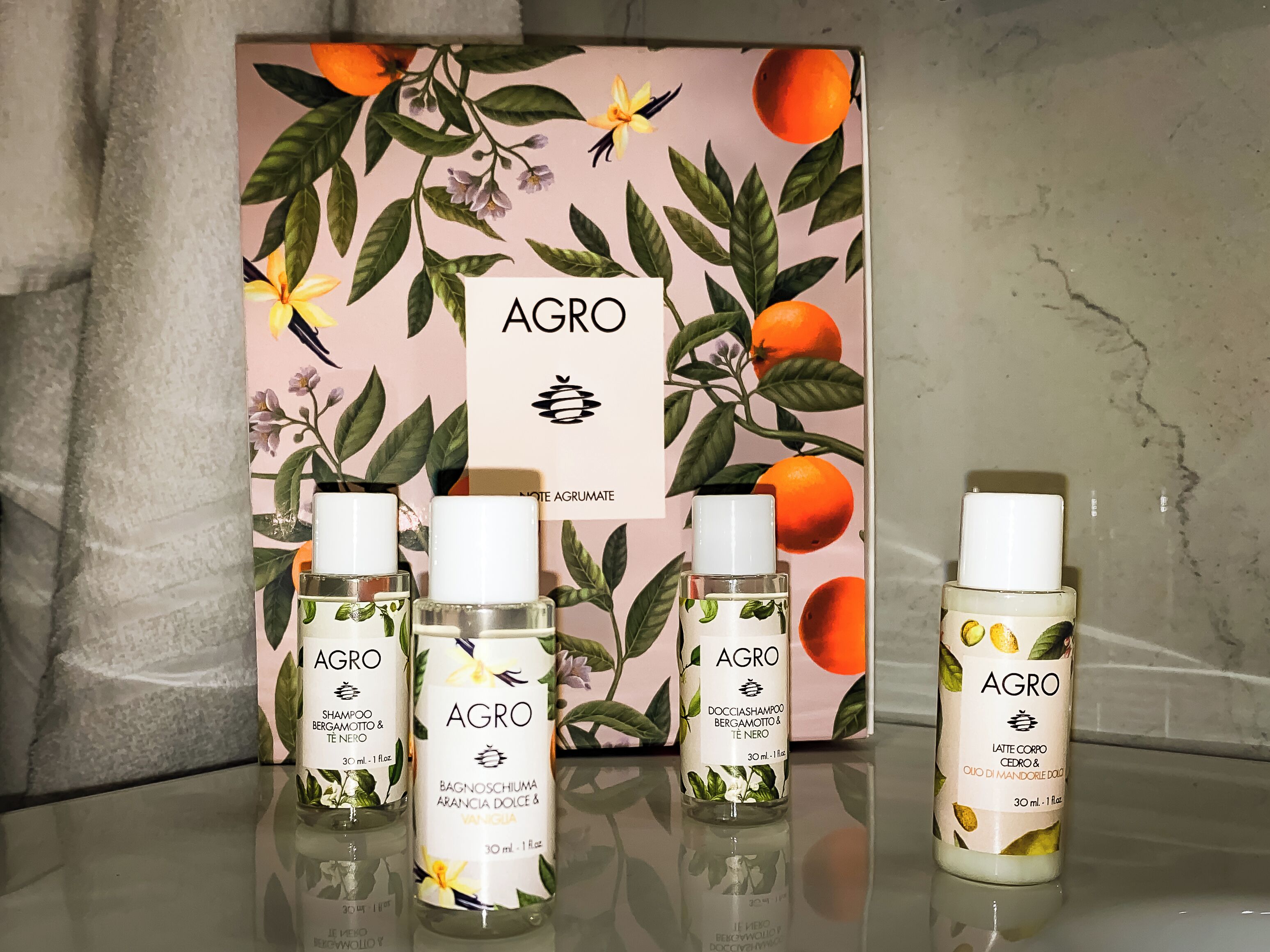 Vier flessen AGRO shampoo en conditioner, geplaatst voor een doos met bloemendecor.