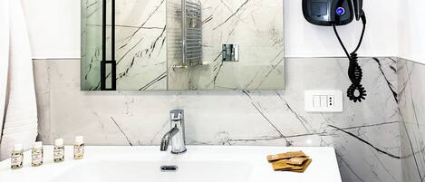 A bathroom with a white sink, a mirror, a hairdryer, and toiletries on the counter.