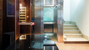 An elevator with a glass door, a red emergency button, and a control panel with a red light. - Suiteincenter Rooms (Palermo)