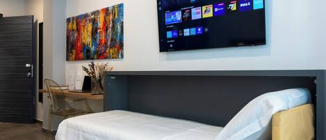 A modern hotel room with a bed, a desk, a flat-screen TV, and a colorful abstract painting.