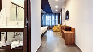 A modern hotel room with a large bed, a wooden desk, a chair, and a view of the city through large windows. - Suiteincenter Rooms (Palermo)