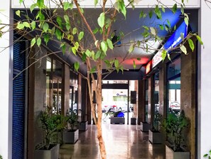 A covered walkway with potted plants, a blue sign, and a visible car in the background. - Suiteincenter Rooms (Palermo)