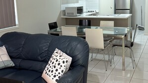 Uma sala de estar moderna com um sofá de couro preto, uma mesa de jantar de vidro e uma cozinha com armários e eletrodomésticos.