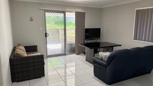 Sala de estar com sofá, televisão, mesinha e porta de vidro deslizante para uma varanda.