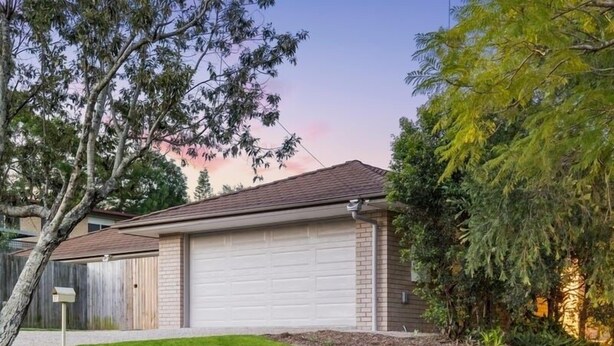 Uma casa com garagem, gramado bem cuidado e árvores já crescidas.
