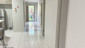 Um corredor com uma área de cozinha à esquerda, uma porta com painel de vidro fosco e um sofá de vime em primeiro plano.