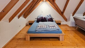Un dormitorio con techo inclinado, vigas de madera, una cama con almohadas, una mesita de noche y un aparador.