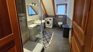 Un baño moderno y compacto con ducha, lavamanos, inodoro y lavadora.