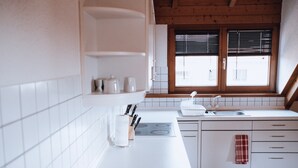 Una cocina con armarios blancos, una estufa y un ventanal con persianas.
