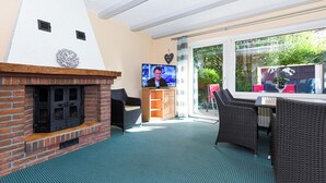 A room with a fireplace, a television, wicker furniture, and a view through a glass door. - Double room incl. breakfast on the North Sea coast (Esens)