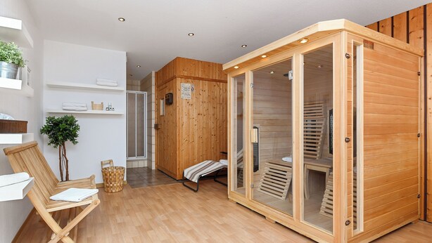 A modern room with a wooden sauna, a wooden bench, a plant, and a shelf with towels. - Double room incl. breakfast on the North Sea coast (Esens)