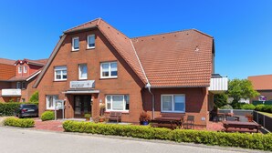 A red-brick building with a sign reading 'Pension Nordkap,' outdoor seating, and a clear blue sky. - Double room incl. breakfast on the North Sea coast (Esens)