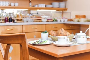Ein Frühstückstisch gedeckt mit Tellern, Besteck, Brot, einer Tasse und einer Karaffe.