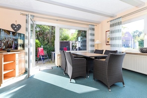 A dining area with wicker furniture, a table, and chairs, a television, and a view of the outdoors. - Double room incl. breakfast on the North Sea coast (Esens)