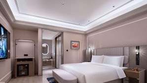 A modern hotel room with a large bed, a bedside table, a built-in TV, and a bathroom with a mirror and sink.