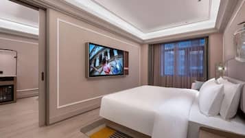 A modern hotel room with a large bed, a flat-screen TV mounted on the wall, and a bedside table with a lamp.