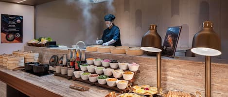 Montaje de bufé con diversas opciones de comida y un chef preparando alimentos.