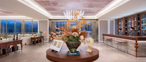 A hotel lobby with a reception desk, a large window, and a decorative table with a vase of flowers.