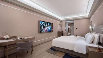 Ein modernes Hotelzimmer mit Bett, Schreibtisch, Stuhl, Fernseher und einem durch eine geöffnete Tür einsehbaren Badezimmer.