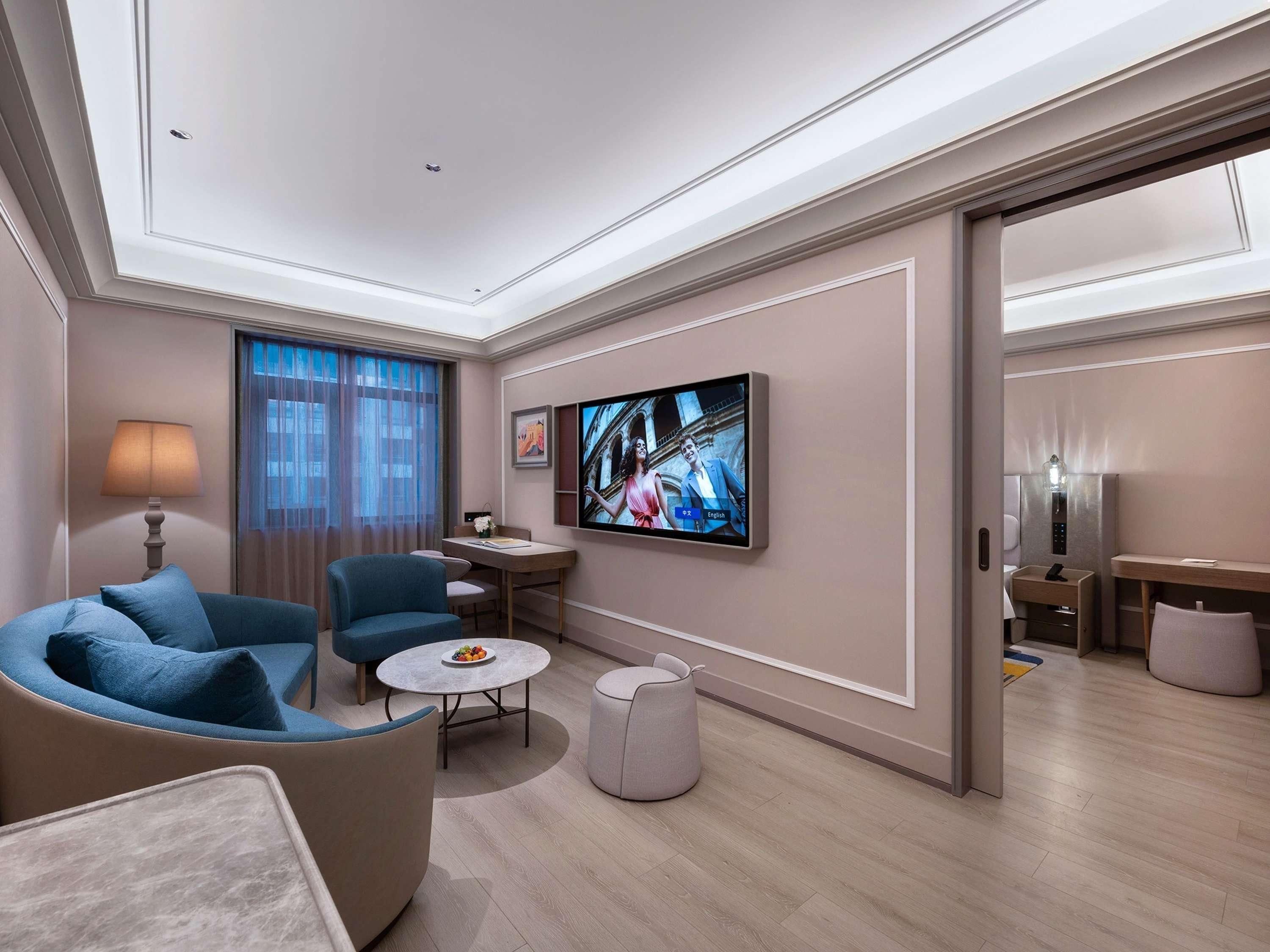 Ein modernes Hotelzimmer mit einer Couch, einem Sessel, einem kleinen runden Tisch und einem an der Wand befestigten Fernseher.