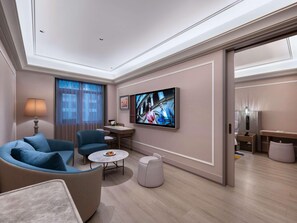 Een moderne hotelkamer met een bank, fauteuil, klein rond tafeltje en een aan de muur bevestigde televisie.