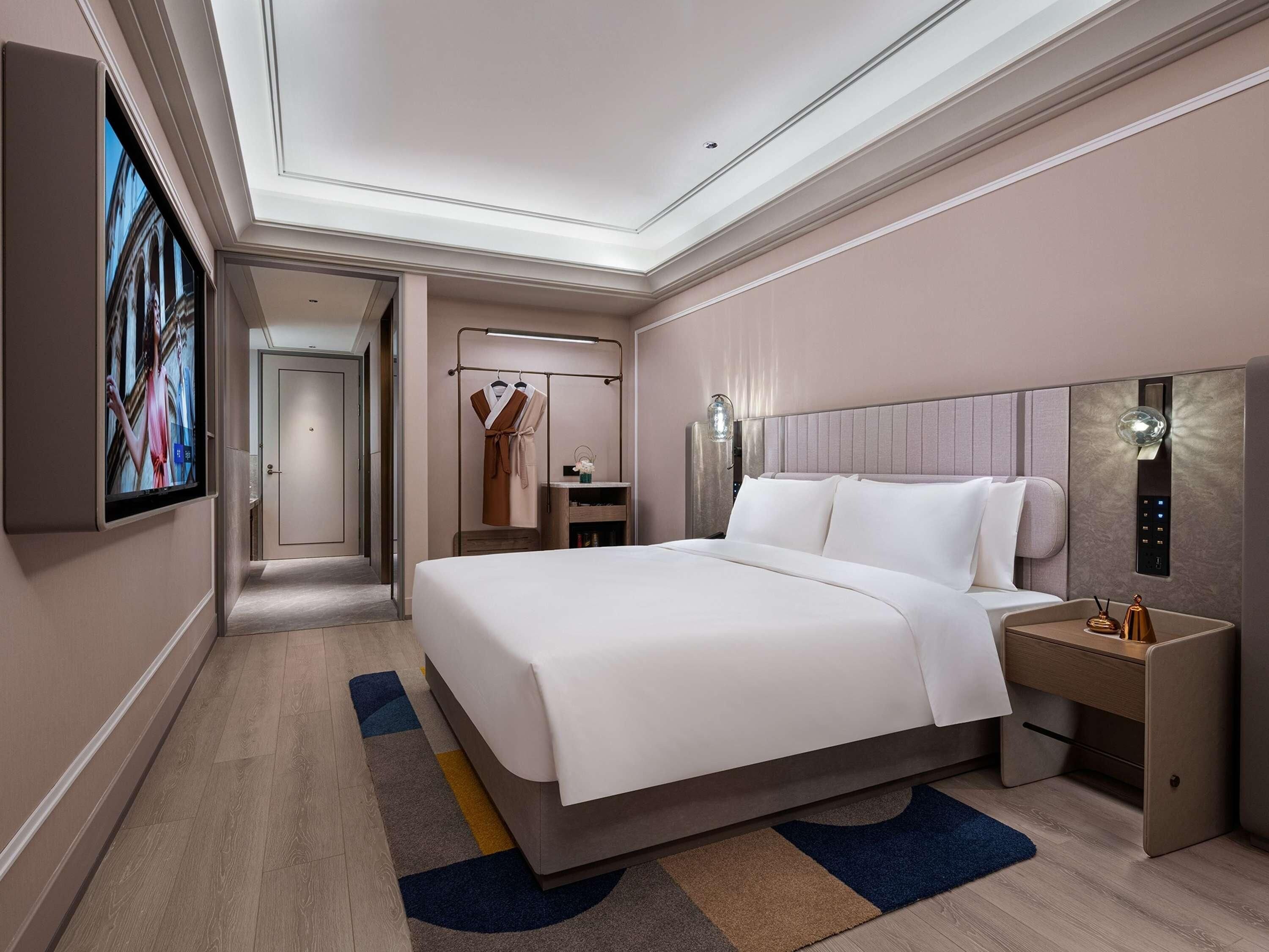 A modern hotel room with a large bed, bedside tables, a TV, and a wardrobe.