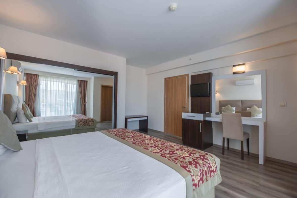 A hotel room with a bed, a desk, a chair, a TV, and a window with curtains.