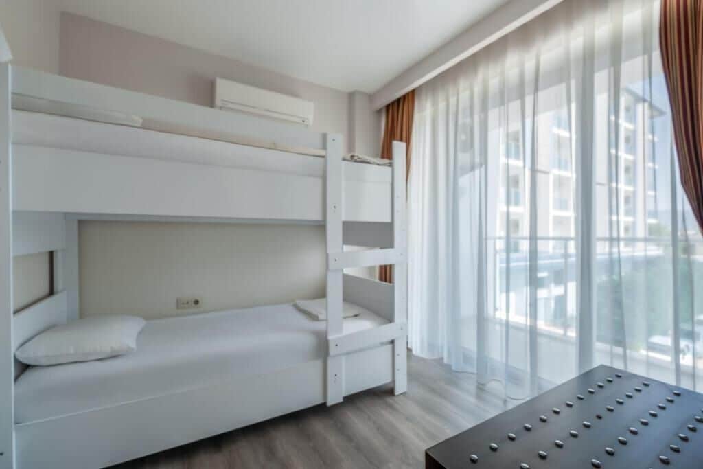 A bunk bed room with a window, a bedside table, and a curtain.