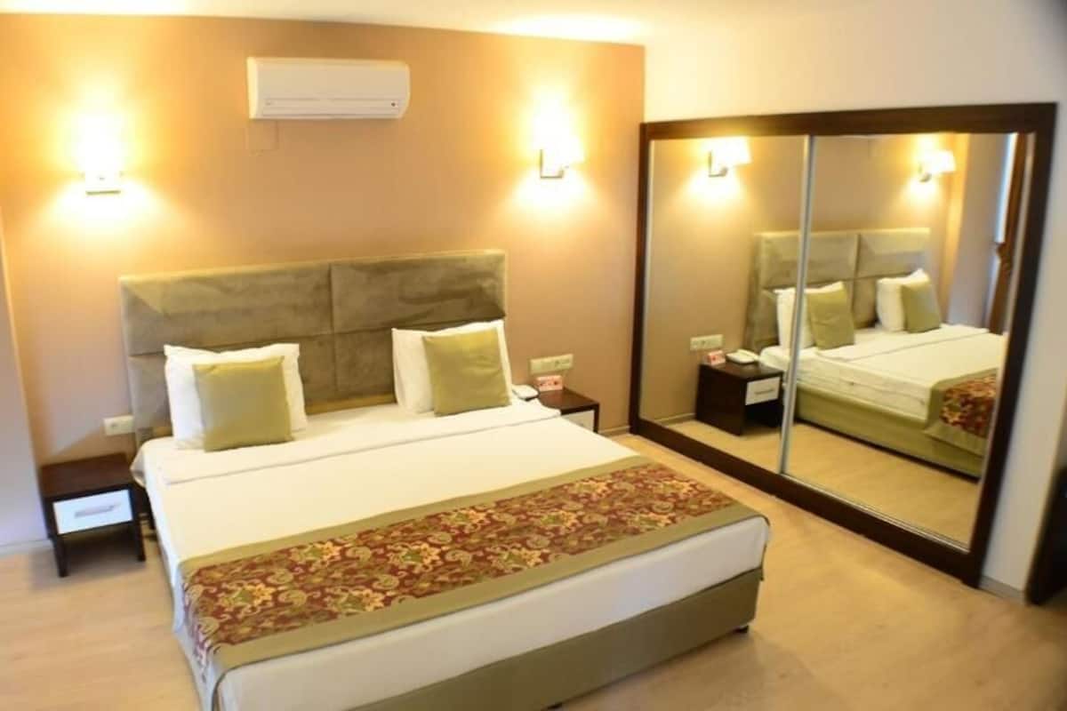 A hotel room with a bed, bedside tables, a mirror, and an air conditioning unit.