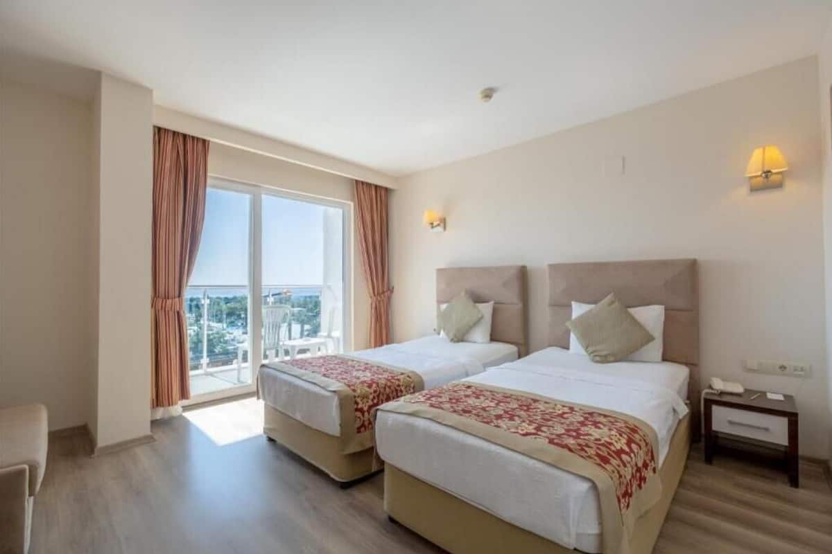 A hotel room with two beds, a balcony, and a view of the city.