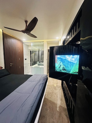 A bedroom with a bed, a television, a ceiling fan, and a bathroom visible through an open door.