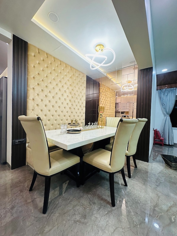 A dining area with a tufted headboard, a marble floor, and a modern chandelier.