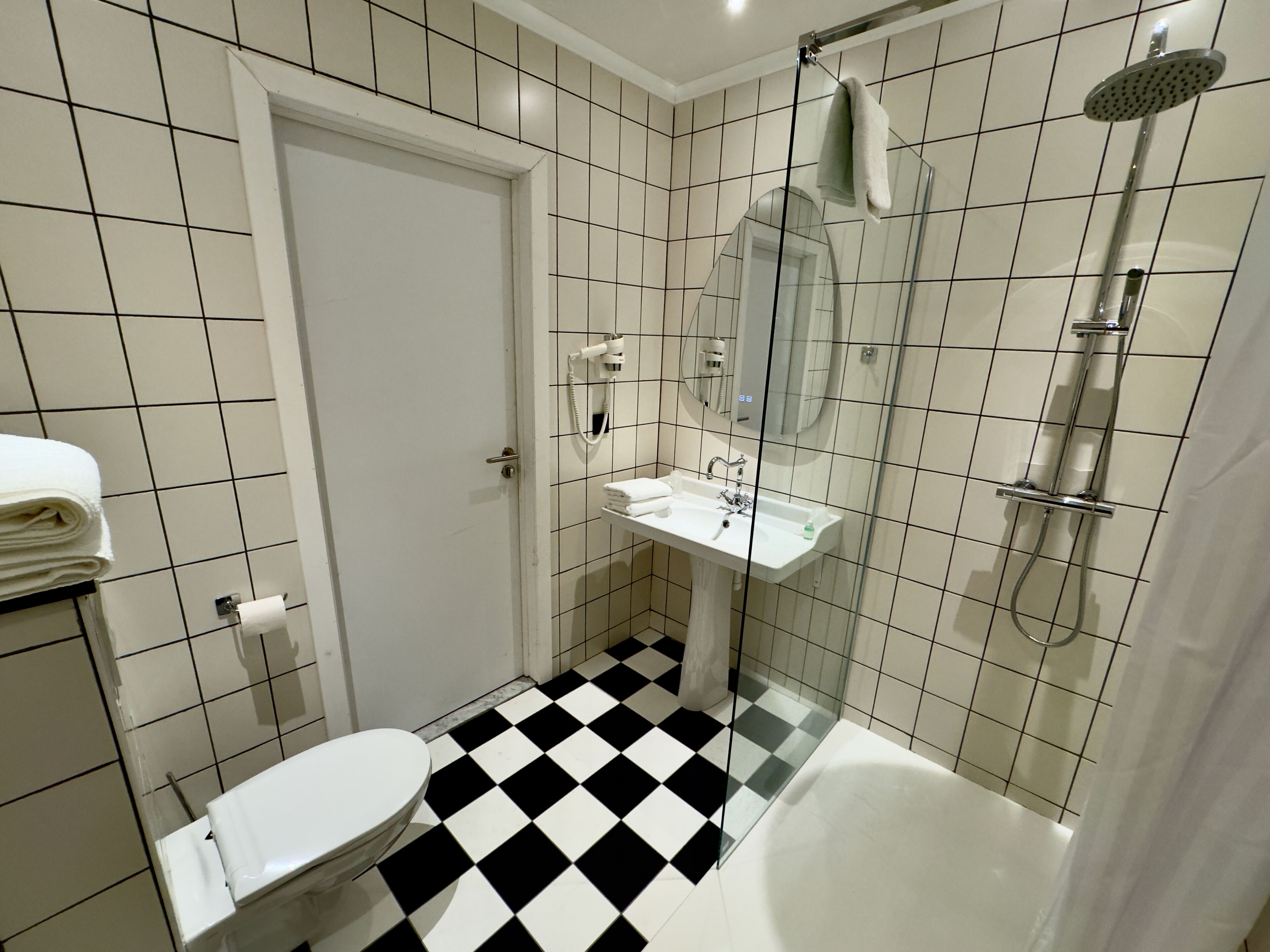 Une salle de bain avec un carrelage à motifs géométriques, des toilettes blanches, un lavabo avec un miroir et une douche.