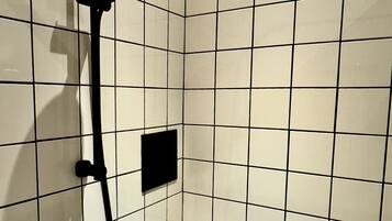 Ducha con cabezal de ducha de mano y accesorio de ducha manual, todo montado en una pared con azulejos.