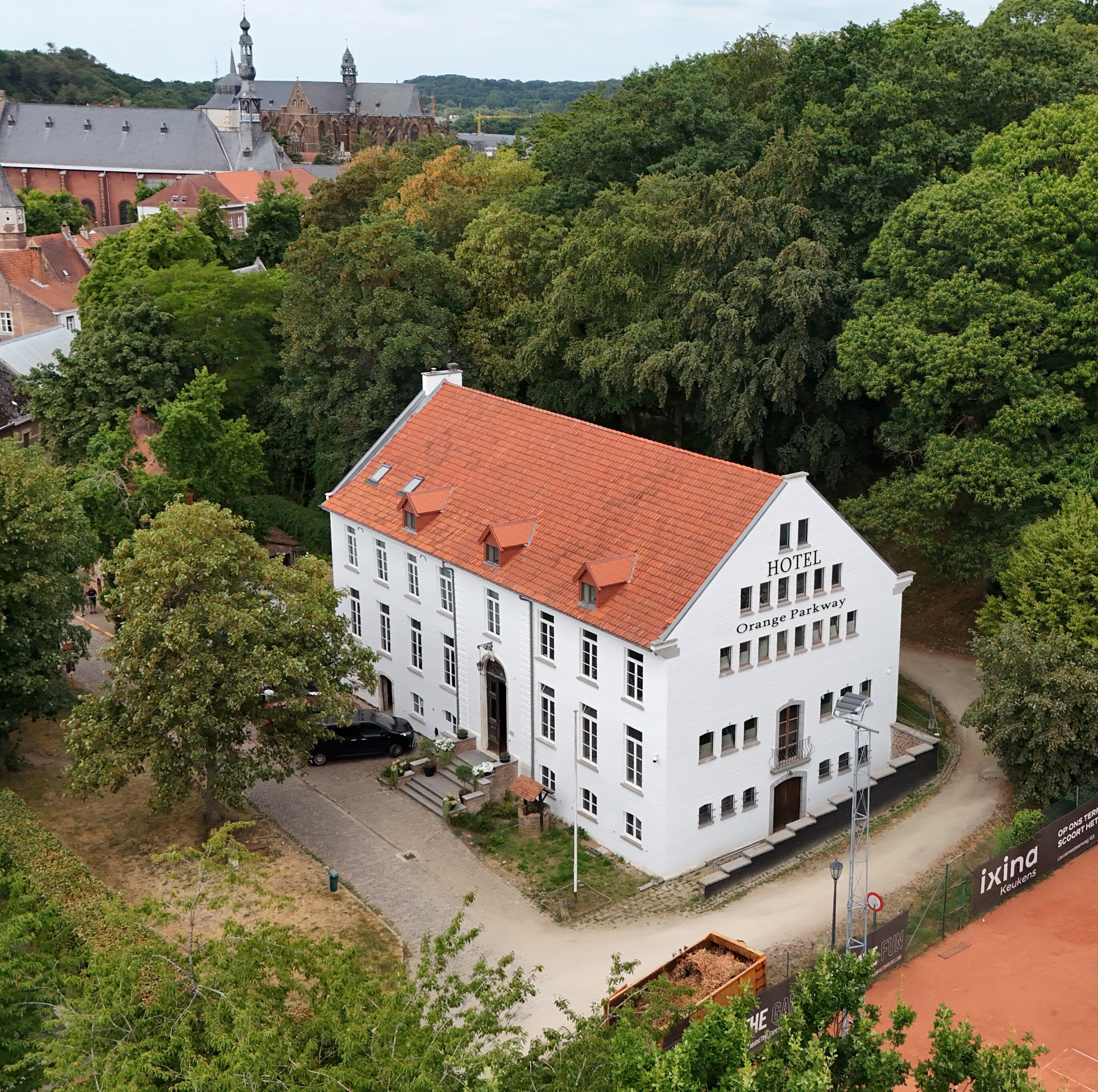 A white building with a red roof, labeled 'HOTEL Orange Parkway,' surrounded by lush greenery.