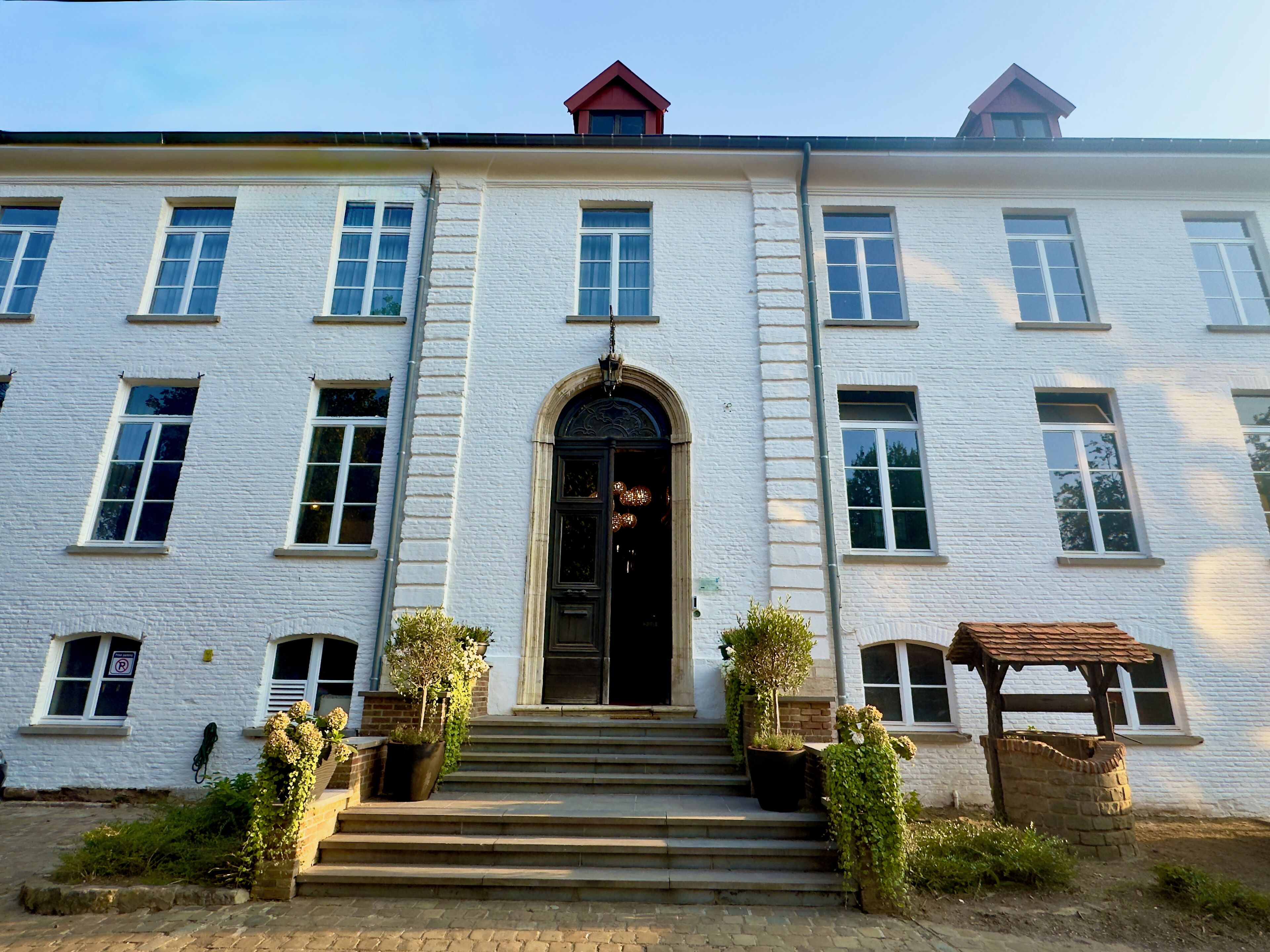 Un bâtiment blanc doté d’une entrée centrale, de nombreuses fenêtres et d’un petit jardin avec des marches menant à l’entrée.