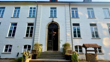 Un bâtiment blanc doté d’une entrée centrale, de nombreuses fenêtres et d’un petit jardin avec des marches menant à l’entrée.