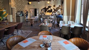 Een restaurantinterieur met houten tafels, stoelen en hangende lampen.