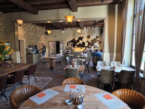A restaurant interior with wooden tables, chairs, and hanging pendant lights. - Orange Parkway (Diest)