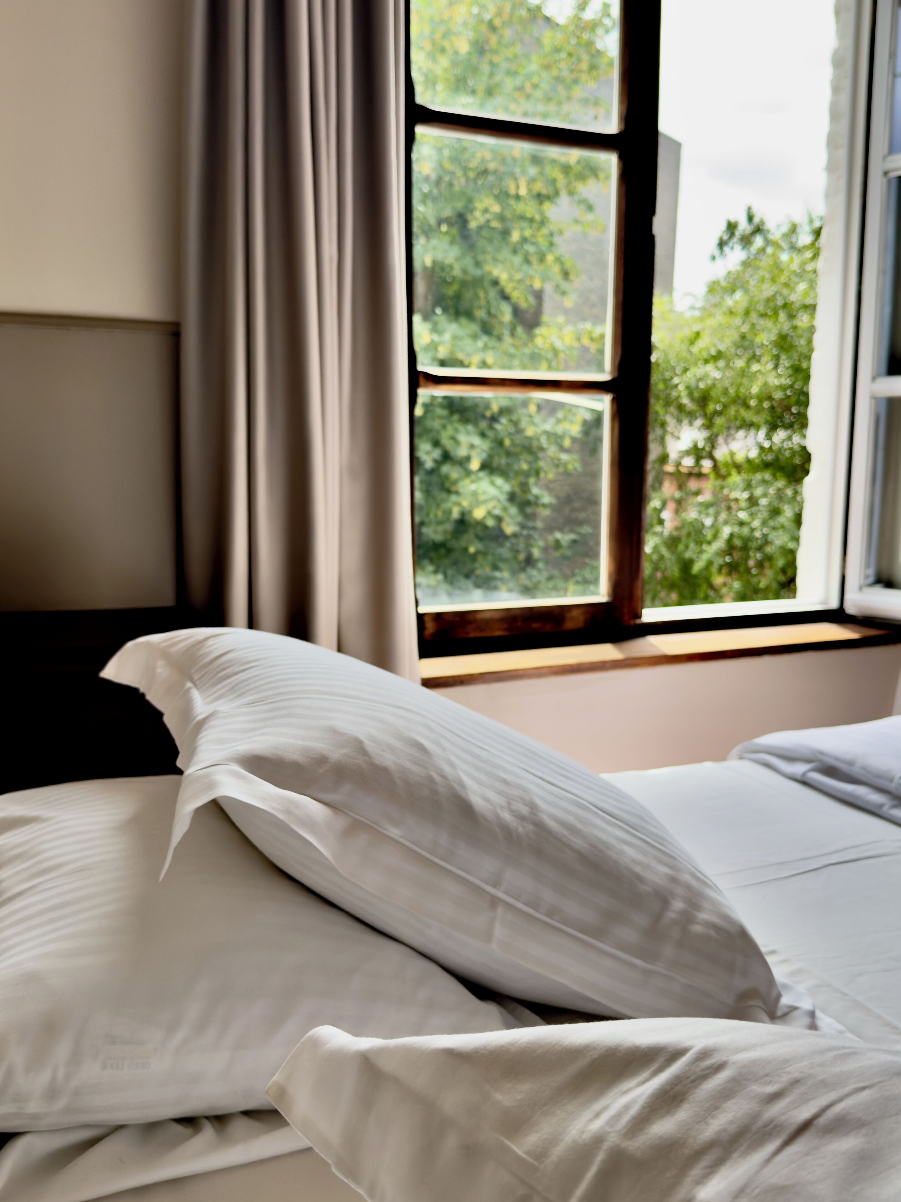 A bedroom with a bed, a window with curtains, and a view of greenery outside.