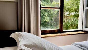 A bedroom with a bed, a window with curtains, and a view of greenery outside.