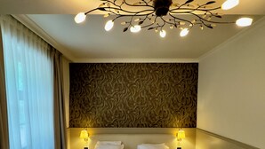 Een hotelkamer met een groot bed, twee bedlampen, een decoratieve plafondlamp en een behang met patroon.