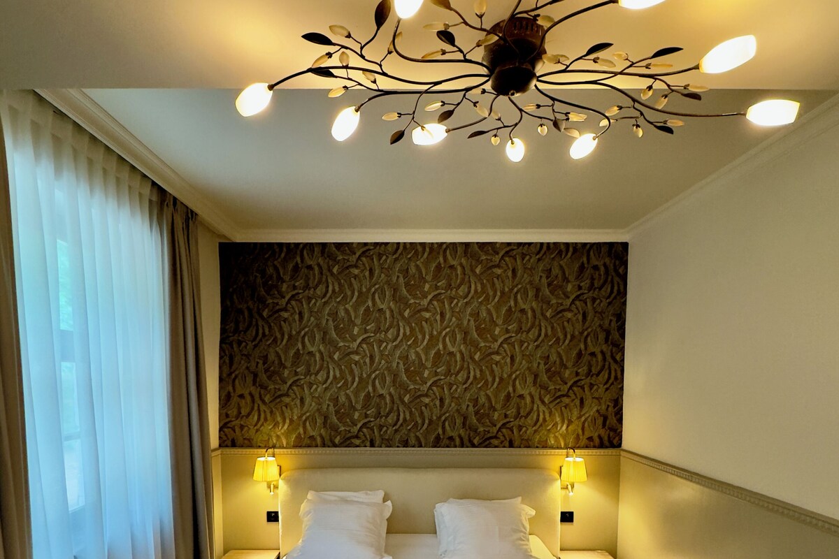 A hotel room with a large bed, two bedside lamps, a decorative ceiling light, and a patterned wall.
