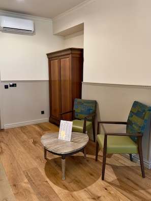 A room with a round wooden table, two chairs, a wooden wardrobe, and a wall-mounted air conditioning unit.