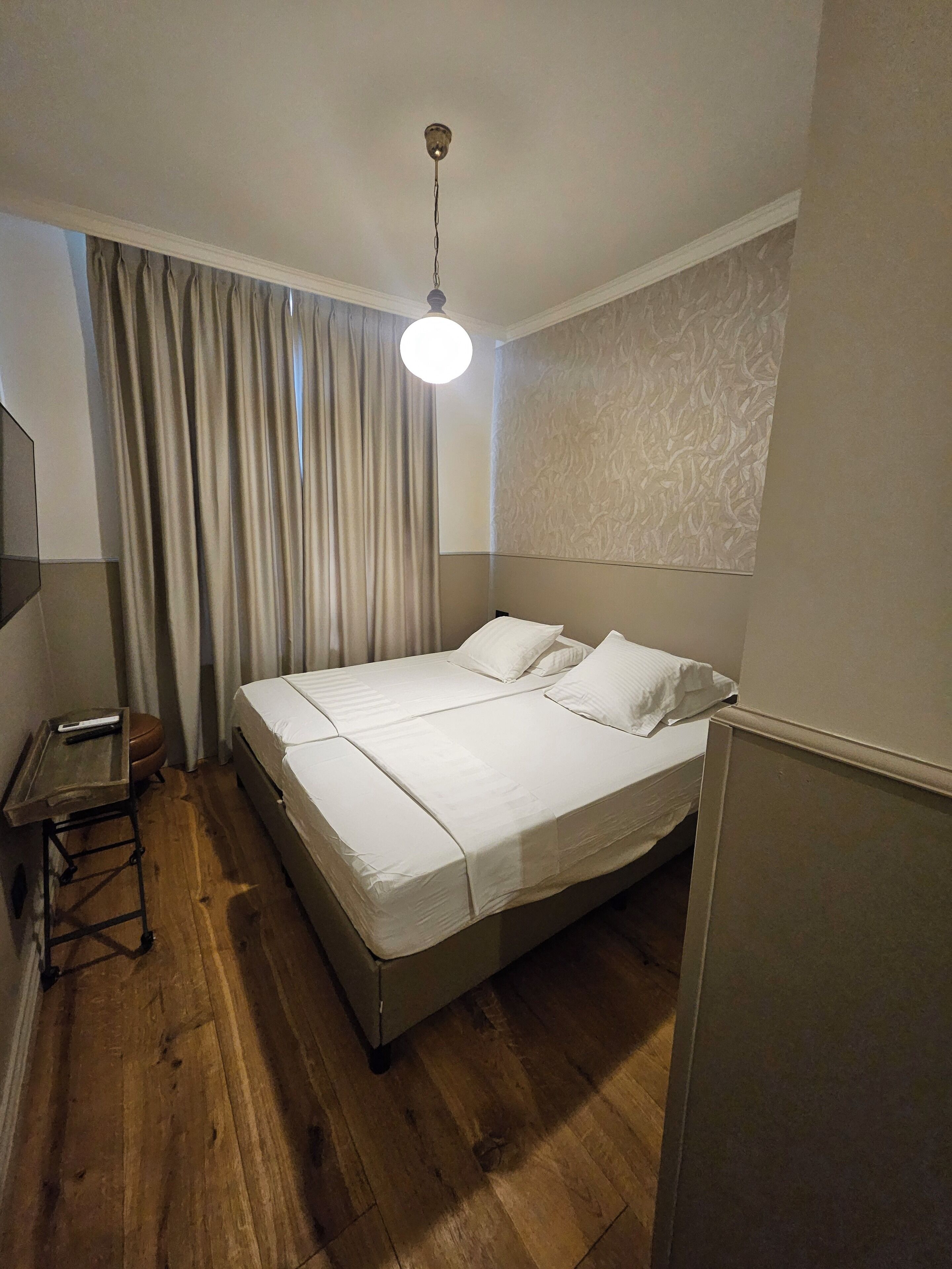 Een hotelkamer met een bed, bureau, stoel, televisie en gordijn.